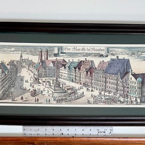 May include: A framed black and white print of a city square with buildings and people. The print is titled "Der Markt zu Munchen".