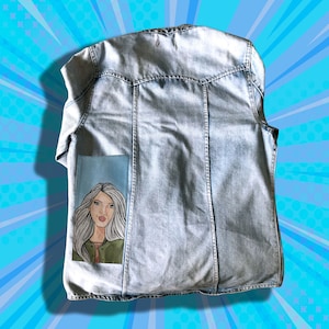 May include: A light blue denim jacket with a painted image of a woman with long blonde hair on the back pocket.