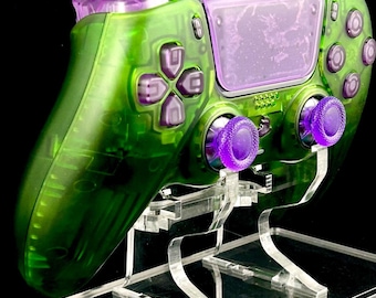 May include: A green and purple translucent video game controller with purple buttons and analog sticks, displayed on a clear acrylic stand.