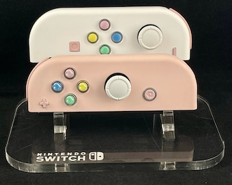 Joy-Cons de Nintendo personalizados en blanco y rosa con corazones de arcoíris y detalles en rosa.