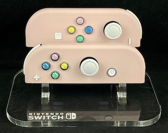 Joy-Cons de Nintendo en color rosa flor de cerezo con botones de corazón arcoíris y detalles en blanco