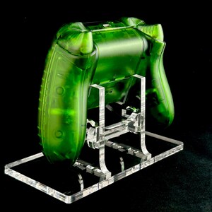 May include: A clear green video game controller on a clear acrylic stand. The controller is translucent and has a textured surface.