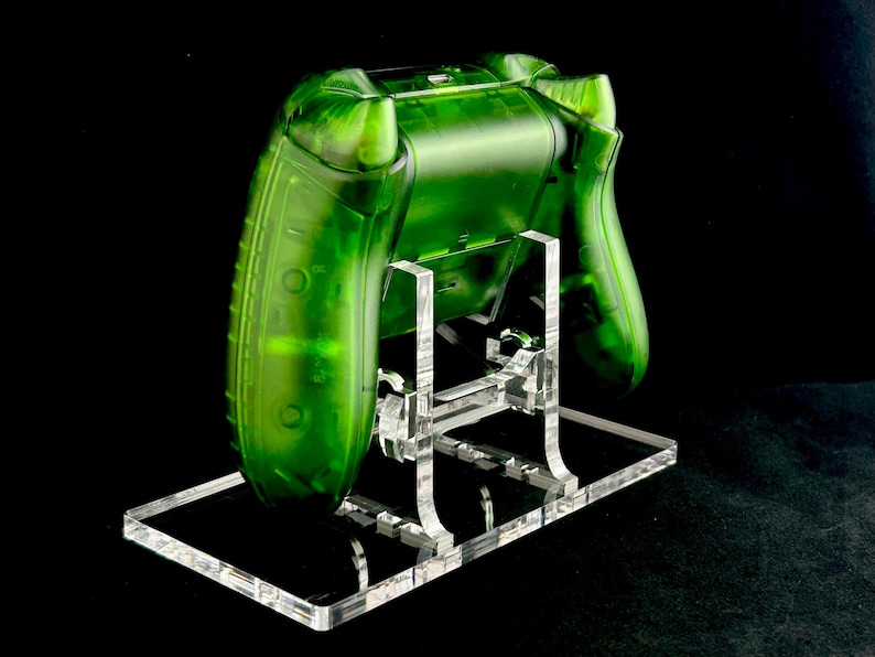 May include: A clear green video game controller on a clear acrylic stand. The controller is translucent and has a textured surface.