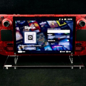 Puede incluir: Un dispositivo de juego portátil rojo con una pantalla que muestra una página de inicio de sesión para una plataforma de juegos. La pantalla muestra un código QR, un campo de nombre de usuario y contraseña, y botones para "Iniciar sesión", "Crear cuenta" y "Cancelar".