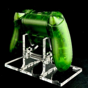 May include: A clear green video game controller on a clear acrylic stand. The controller is translucent and shows the internal components.
