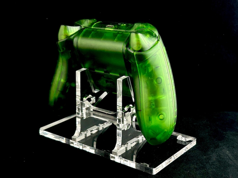 May include: A clear green video game controller on a clear acrylic stand. The controller is translucent and shows the internal components.