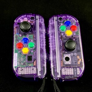 Pu&ograve; includere: Una coppia di controller Nintendo Switch Joy-Con trasparenti viola con pulsanti colorati. I controller hanno un guscio in plastica trasparente, che rivela i componenti interni.