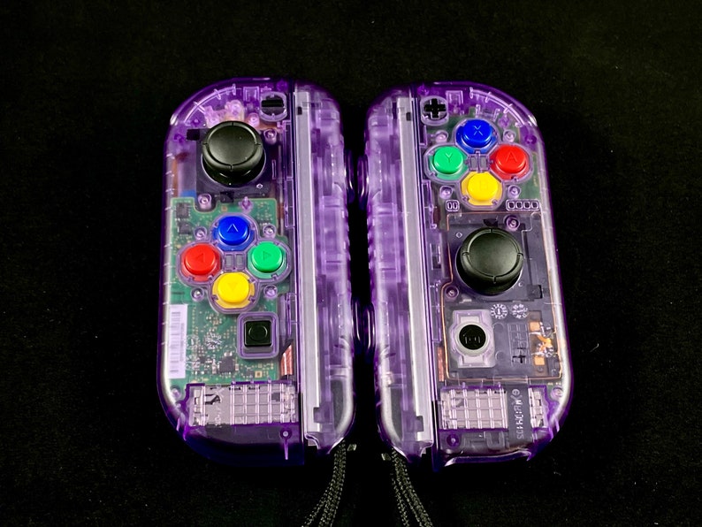 Pu&ograve; includere: Una coppia di controller Nintendo Switch Joy-Con trasparenti viola con pulsanti colorati. I controller hanno un guscio in plastica trasparente, che rivela i componenti interni.