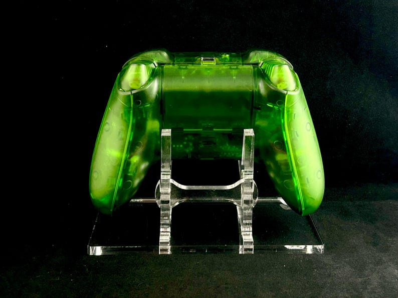May include: A clear green video game controller on a clear acrylic stand. The controller is translucent and shows the internal components.
