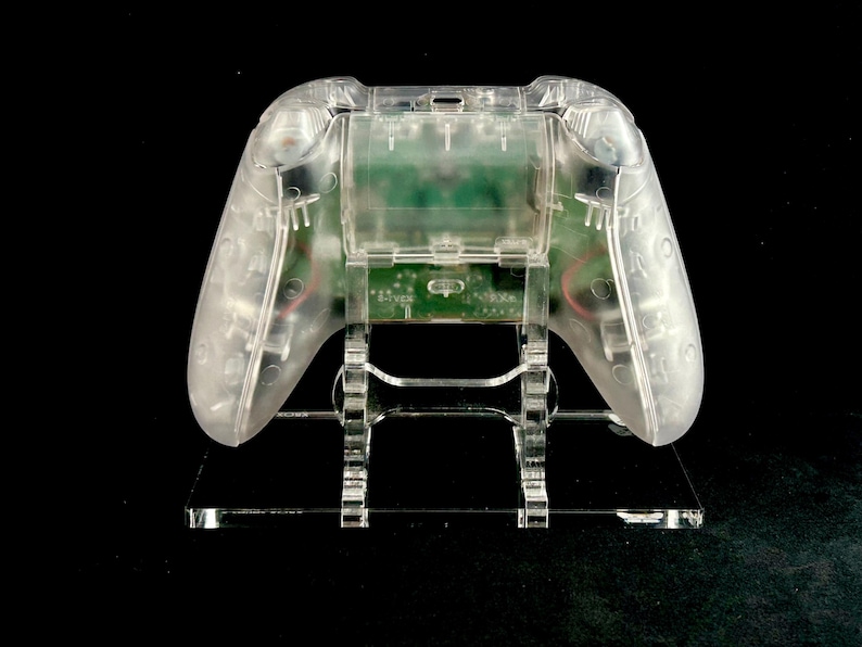 May include: A clear plastic video game controller stand with a clear plastic video game controller on top of it.