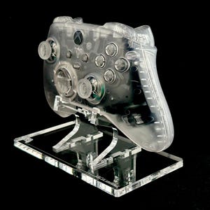 May include: A clear plastic stand with a transparent Xbox controller on top. The controller has a textured surface and is designed to be displayed.