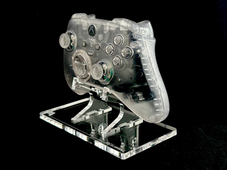 May include: A clear plastic stand with a transparent Xbox controller on top. The controller has a textured surface and is designed to be displayed.