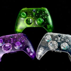 May include: Three clear plastic Xbox controllers in different colors: green, purple, and clear. The controllers are translucent and show the internal components.