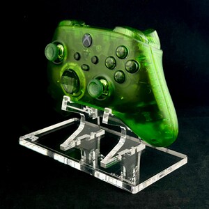 May include: A clear green Xbox controller on a clear acrylic stand. The controller has a translucent green color and is displayed on a clear acrylic stand.