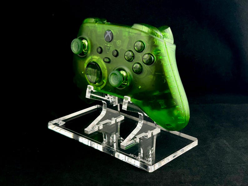 May include: A clear green Xbox controller on a clear acrylic stand. The controller has a translucent green color and is displayed on a clear acrylic stand.