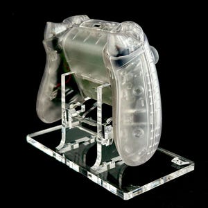 May include: A clear plastic video game controller on a clear acrylic stand. The controller is designed for a video game console.