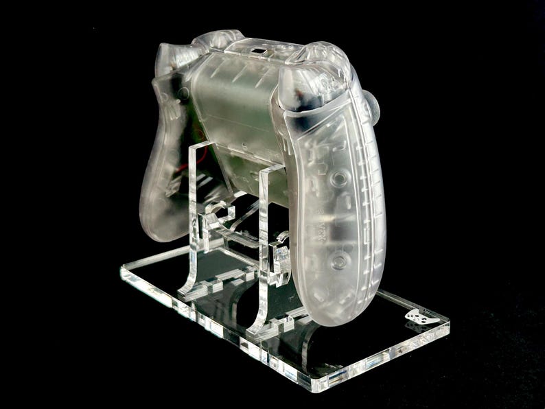 May include: A clear plastic video game controller on a clear acrylic stand. The controller is designed for a video game console.