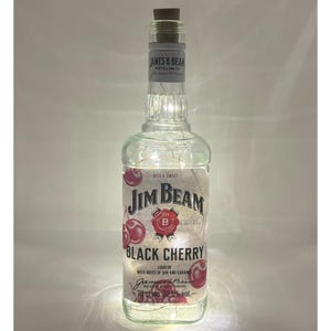 May include: A clear glass bottle with a cork top and a label that reads "Jim Beam Black Cherry" with a red cherry graphic. The bottle is filled with white LED lights.
