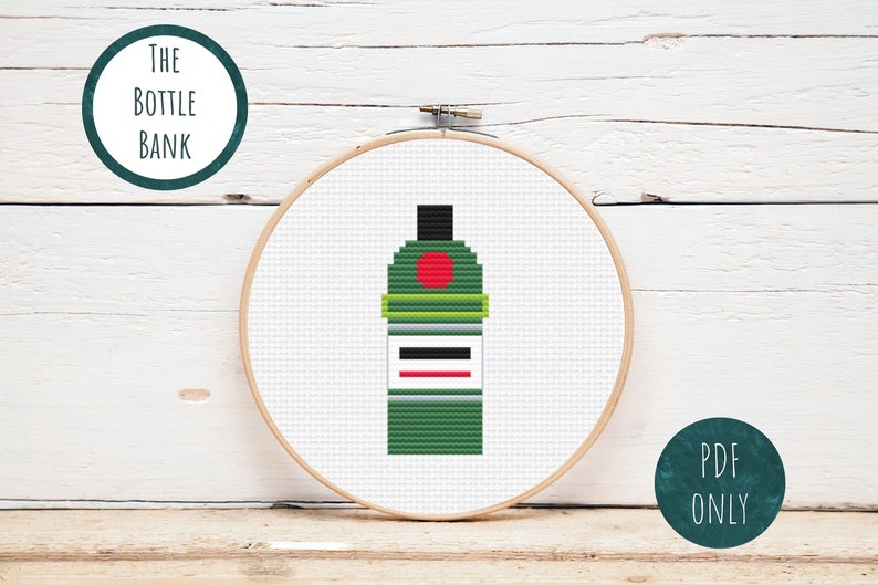 May include: A cross-stitch pattern of a green bottle with a red circle and a white label. The pattern is in a wooden embroidery hoop. The text "THE BOTTLE BANK" is in a circle above the hoop and "PDF ONLY" is in a circle below the hoop.