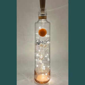 May include: A clear glass bottle with a wooden cork top, filled with white fairy lights. The bottle is labelled "CIROC Mango Flavoured Vodka".