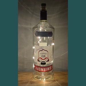 May include: A clear glass bottle with a red and white label that says "Smirnoff No. 21 Vodka". The bottle is decorated with white fairy lights.