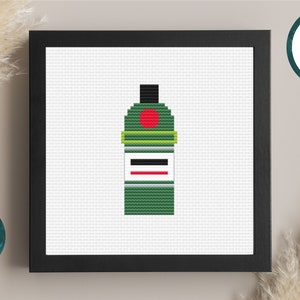 May include: A cross-stitch pattern of a green bottle with a red circle and a white label. The pattern is framed in a black frame.