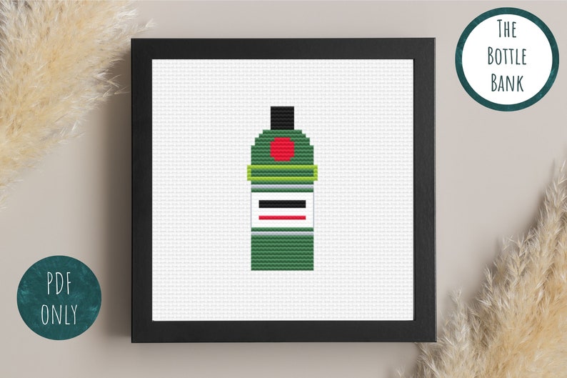 May include: A cross-stitch pattern of a green bottle with a red circle and a white label. The pattern is framed in a black frame.