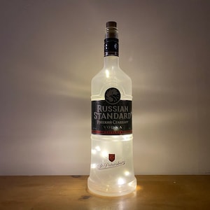 May include: A clear glass bottle with a frosted finish and a label that reads "Russian Standard Vodka". The bottle is decorated with small white lights.