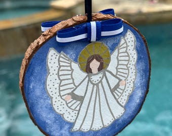 May include: A blue and white painted wooden angel ornament with a blue and white ribbon. The angel has a halo and is painted in a simple style.