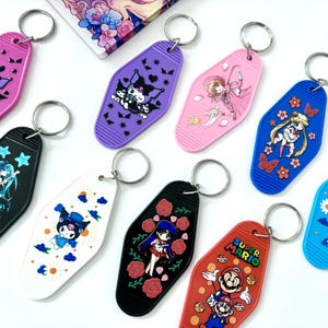 May include: A set of ten colorful keychains featuring various cartoon characters. Each keychain is shaped like a motel key tag and has a metal ring for attaching to keys. The characters include Sailor Moon, Super Mario, and various anime characters.