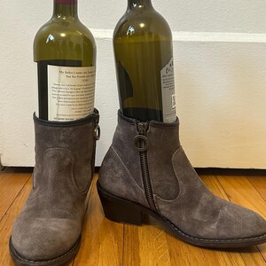 May include: A pair of gray suede ankle boots with a zipper on the side. The boots have a low heel and are worn with wine bottles inside.