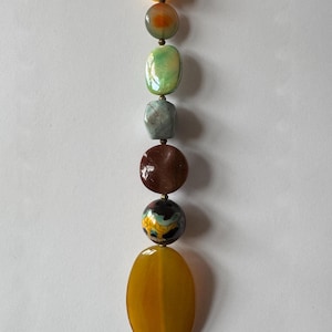 May include: A strand of colorful beads in various shapes and sizes. The beads include yellow, orange, green, blue, brown, and a patterned bead. The largest bead is an oval shape, and the smallest is a small yellow rectangle.