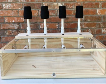 May include: A wooden box with a clear plastic lid and four black foam targets on top. The targets are attached to white PVC pipes that extend down into the box. The box is sitting on a white surface.