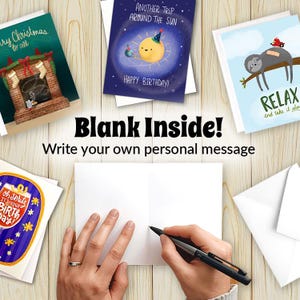 Op de afbeelding: Wenskaarten met diverse ontwerpen, waaronder een open haard, een zon en een luiaard. De kaarten zijn blanco van binnen, met de tekst "Blank Inside! Write your own personal message". Een hand schrijft met een pen in een kaart.