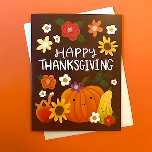 May include: A brown card with a Happy Thanksgiving message surrounded by colourful flowers and a smiling pumpkin with a squash beside it.