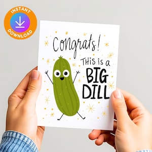 May include: A greeting card with the words "Congrats! This is a BIG DILL" and a cartoon pickle character. The card has a white background with gold star accents and is held by hands.