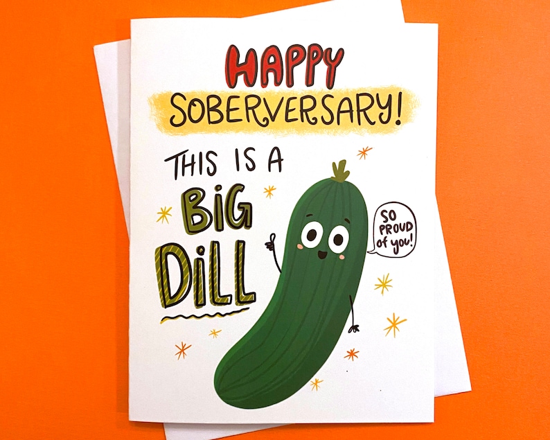 Pu&ograve; includere: Un biglietto bianco con un cetriolo di cartone animato verde con un viso e le braccia. Il biglietto dice "Happy Soberversary! This is a Big Dill. So proud of you!"