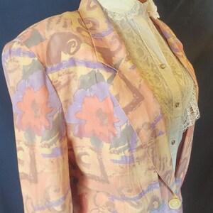 May include: A pink, yellow, and purple floral patterned blazer with a single button closure. The blazer is on a mannequin with a white lace blouse.