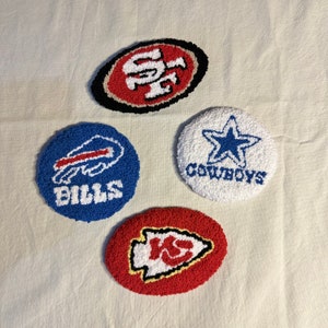 May include: Four round, colourful, embroidered patches with different NFL team logos. The logos are for the San Francisco 49ers, Buffalo Bills, Dallas Cowboys, and Kansas City Chiefs.