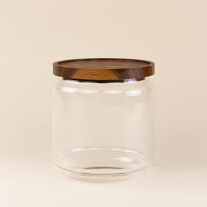 May include: A clear glass jar with a wooden lid. The lid is a dark brown color and has a smooth, polished finish.