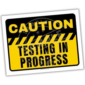 Può includere: Un cartello rettangolare con sfondo nero e testo giallo che recita "CAUTION TESTING IN PROGRESS". Il cartello ha un bordo a strisce gialle e nere e si trova su uno sfondo bianco.