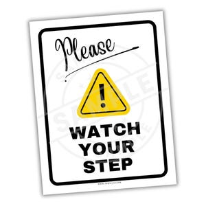 May include: A white rectangular sign with a black border. The sign features the word "Please" in cursive, a yellow triangle with an exclamation mark, and the words "WATCH YOUR STEP" in bold, black letters.