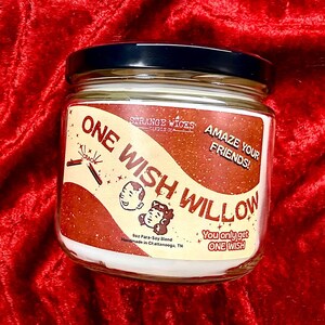 May include: A clear glass candle jar with a black lid and a cream-colored label featuring the text ONE WISH WILLOW, AMAZE YOUR FRIENDS!, and You only get ONE WISH. The label includes illustrations of a wishbone and two cartoon faces.