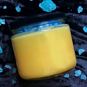 May include: A glass jar with a black lid filled with a yellow substance. The jar is sitting on a black surface with blue crystals scattered around it.