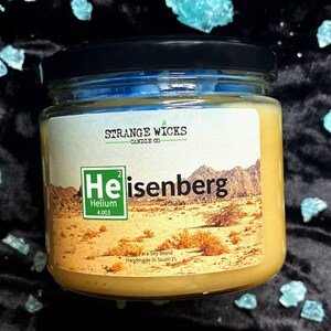 May include: A glass jar candle with a yellow label. The label features a stylized periodic table element for Helium, with the text "Heisenberg" below it. The candle is handmade in South Florida.
