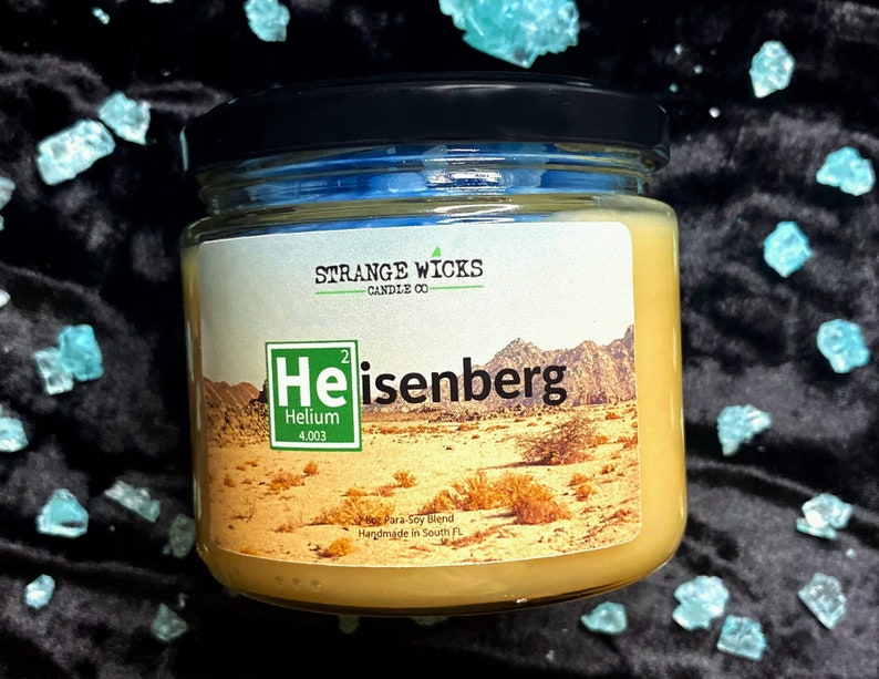 May include: A glass jar candle with a yellow label. The label features a stylized periodic table element for Helium, with the text "Heisenberg" below it. The candle is handmade in South Florida.