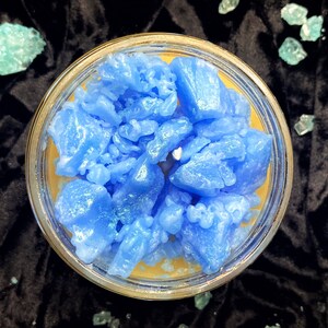 May include: A blue candle with a textured, crystal-like surface. The candle is in a clear glass jar with a yellow wax base.