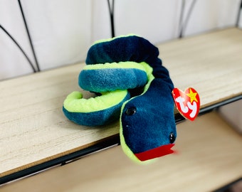 Pode incluir: Um brinquedo de pelúcia de cobra Ty Beanie Baby verde e azul. A cobra está enrolada e tem a língua vermelha para fora. O brinquedo tem uma etiqueta Ty anexada.