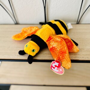 May include: A yellow and black bee plush toy with orange wings and a Ty Beanie Baby tag.