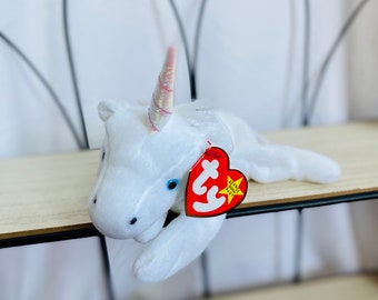 Könnte beinhalten: Weißes Plüsch-Einhorn Beanie Baby mit einem pink-weiß schimmernden Horn und blauen Augen. Das Beanie Baby hat ein rotes Ty-Etikett mit einem weißen Stern und dem Text "Beanie Babies" in weiß.
